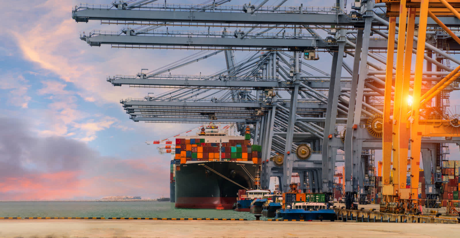 A container vessel alongside quay cranes at sunset.